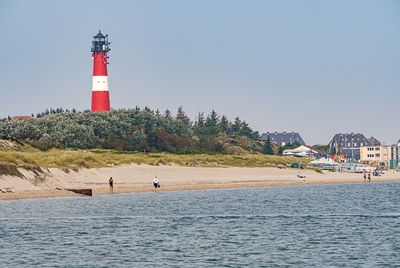 Lighthouse amidst sea and buildings against sky