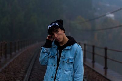 Portrait of young man standing on railway bridge during foggy weather