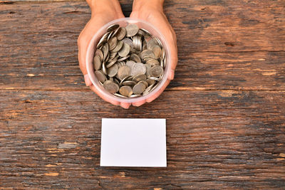 Cropped hands holding container with coins on wooden table