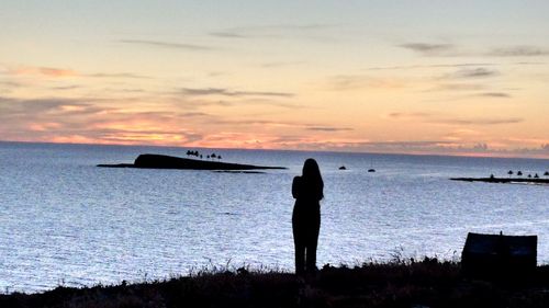 Rear view of silhouette woman standing at beach during sunset