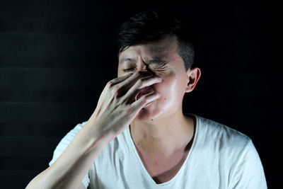 Man covering nose against black background