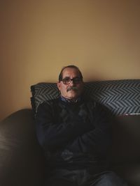 Portrait of mature man sitting on sofa against wall at home