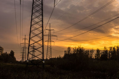 Silhouette electricity pylon against orange sky