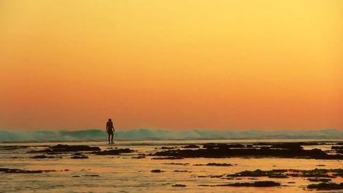 Silhouette man on beach against sky during sunset