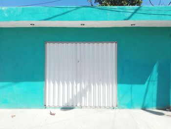 Closed white metallic gate on turquoise wall