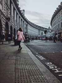 Rear view of woman walking on street against buildings in city