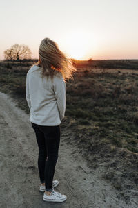 Rear view of woman standing on field against sky during sunset