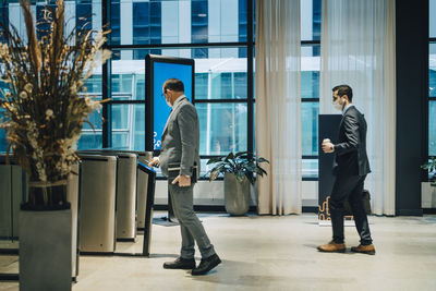 Businessman scanning smart phone to enter subway station while male colleague standing in line during pandemic