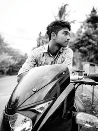 Young man sitting on motorcycle against sky