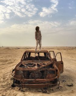 Woman standing on a roof of the burnt car in the desert.
