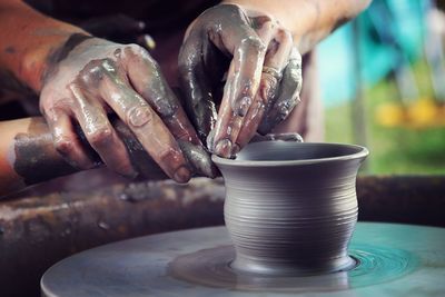 Cropped hands shaping clay on pottery wheel