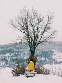 Rear view of person sitting snow covered landscape against sky