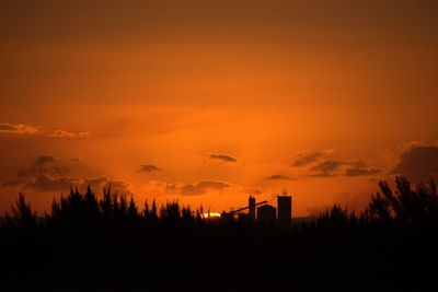 Silhouette of factory against orange sky