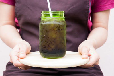 Midsection of woman holding cutting board with mason jar against white background