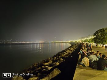 People sitting by river against clear sky at night
