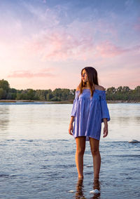 Rear view of young woman standing in lake against sky