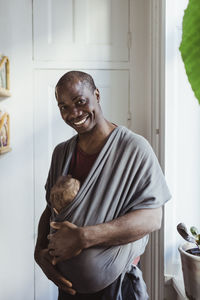 Portrait of happy father with toddler son in carrier at home