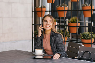 Young charming woman calling on a mobile phone while sitting alone in a cafe and talking