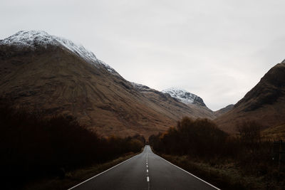 Road leading towards mountains against sky