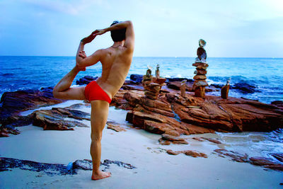 A man in intermediate yoga posure on the stoney beach