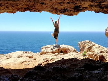 Rear view of woman with arms raised standing on rock against sea