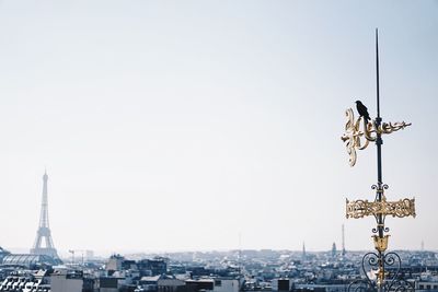 Bird perching on pole with eiffel tower in background against clear sky