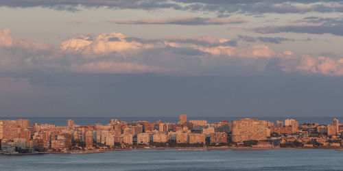 Sea by city buildings against sky during sunset