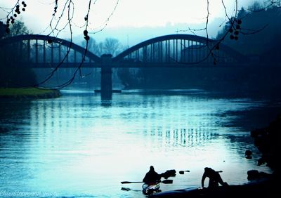 Silhouette men on bridge over river against sky