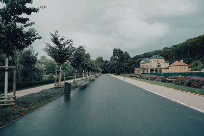 Road amidst trees and buildings against sky