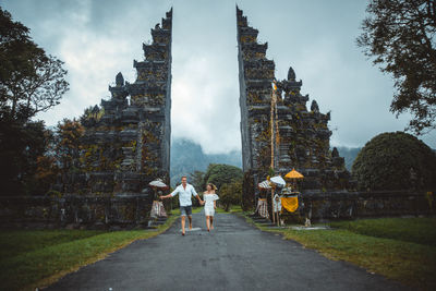 Couple running on footpath at gate against sky