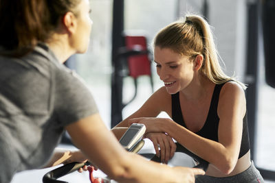 Instructor looking at woman exercising on bike in gym