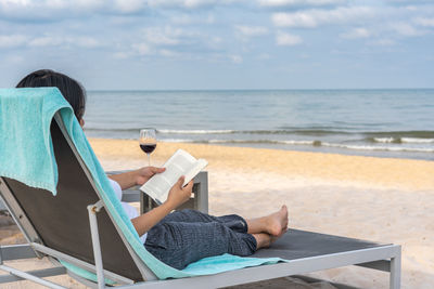 Rear view of woman sitting on lounge chair at beach