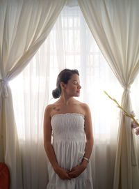 Young woman with eyes closed standing by window at home