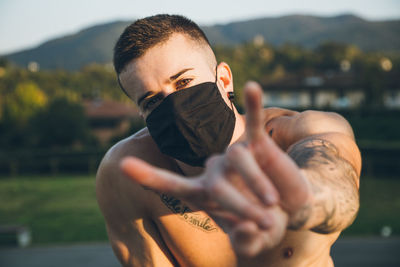 Portrait of shirtless man wearing mask gesturing outdoors