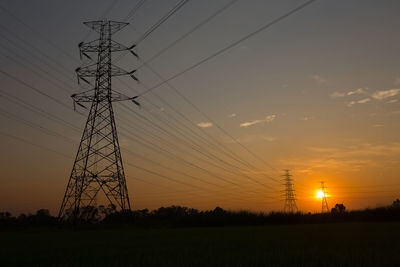 Low angle view of electricity pylon on field against sky during sunset