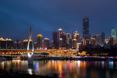 Illuminated buildings by river against sky in city at night