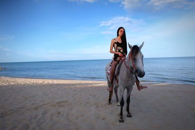 Full length of woman sitting on horse at beach