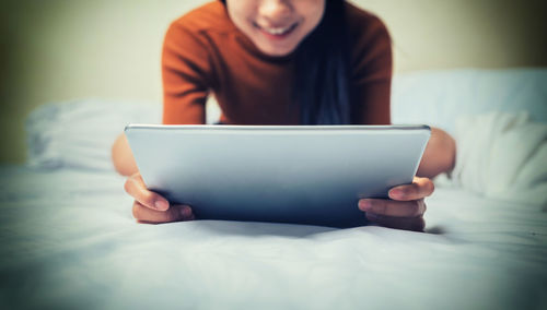 Midsection of man using mobile phone while sitting on bed at home