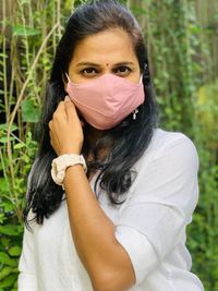Portrait of woman wearing mask standing against plants