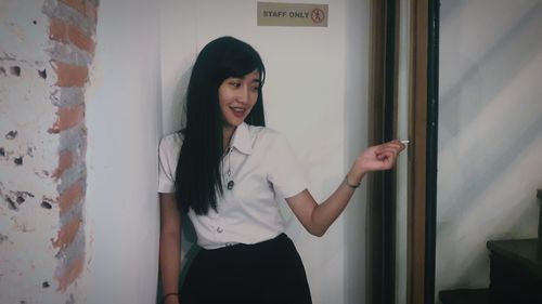 Smiling young woman standing against door at office