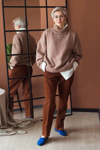 Fashion woman in brown oversize sweater and trousers standing in modern work place or office