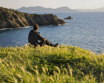 Rear view of woman sitting on rock by sea against mountain