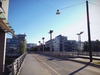 Empty street amidst buildings against clear blue sky