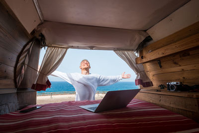 Smiling boy with arms outstretched standing by sea against sky