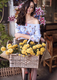 Portrait of woman holding flowers in basket standing outdoors