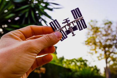 Close-up of hand holding model satellite against sky