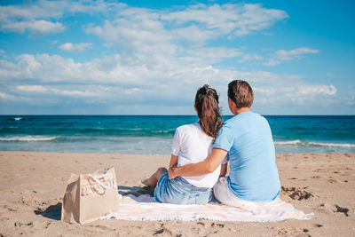 Rear view of woman sitting at beach against sky
