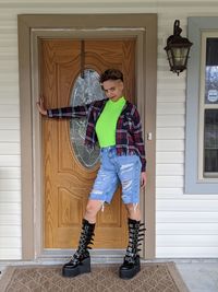 Full length portrait of smiling woman standing against door