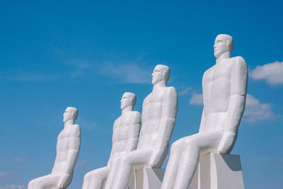 Low angle view of statues against blue sky during sunny day