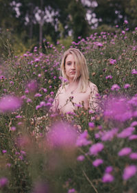 Beautiful young woman standing by purple flowering plants on field